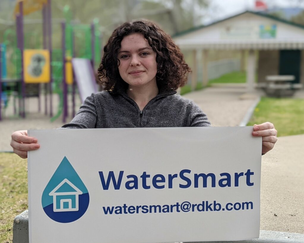 RDKB Water Smart Ambassador, smiling, holding up WaterSmart sign